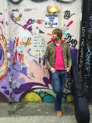 Photo of Lawrence Bray leaning against a graffitied wall.